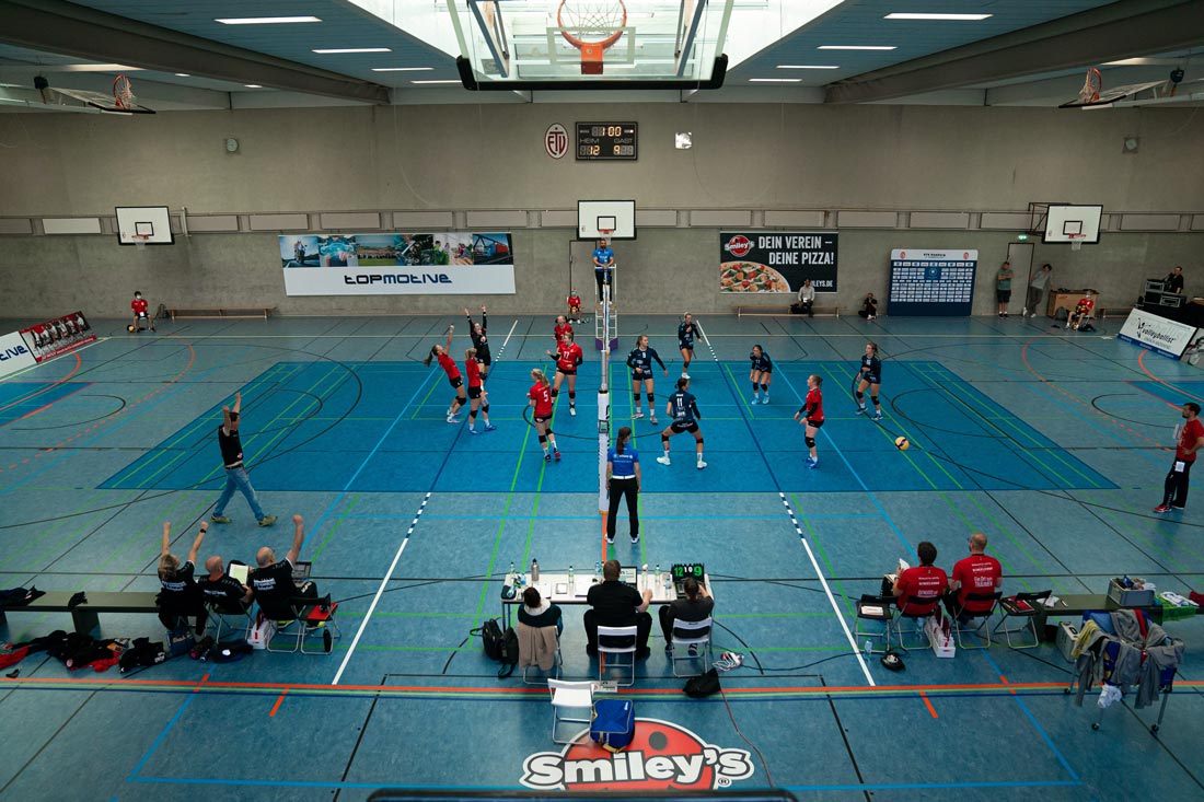Ein Bild einer Damenvolleyballmannschaft mit den neuen, von Smiley's Pizza gesponsorten Trikots während eines Spiels vor einem Smiley's Pizza Banner mit der Aufschrift: Dein Verein - Deine Pizza