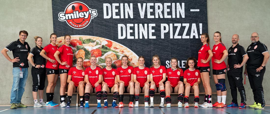 Ein Bild einer Damenvolleyballmannschaft mit den neuen, von Smiley's Pizza gesponsorten Trikots vor einem Smiley's Pizza Banner mit der Aufschrift: Dein Verein - Deine Pizza